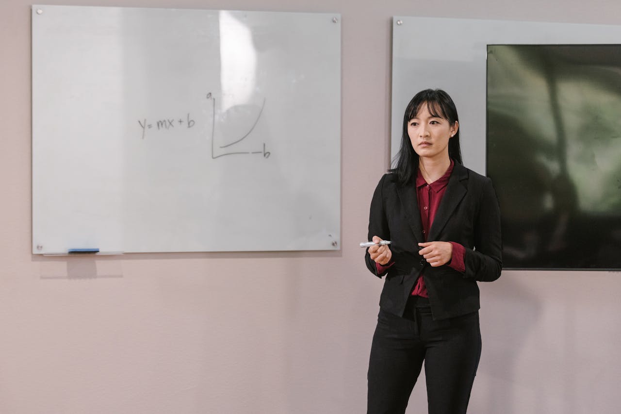 Businesswoman presenting on a whiteboard explaining financial concepts indoors.